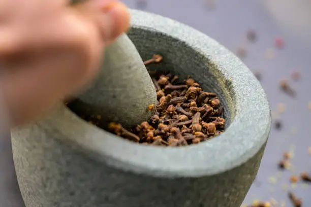 Close-up of cloves being crushed in the mortar with a granite pestle