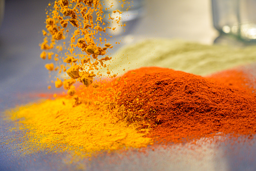 Close-up of turmeric powder falling onto a flat surface next to red chilli powder.