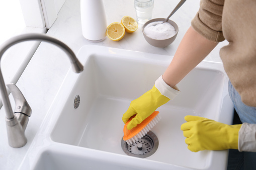 Woman using baking soda and brush to clean sink, closeup