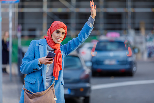 Beautiful Muslim Woman in Rush Hour is Waiting for a Cab. A Traditionally Dressed Muslim Woman with Hijab is Raising his Hand and Trying to Catch a Ride to the Work Place.
