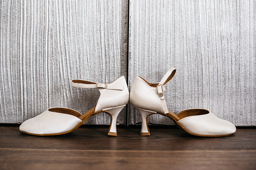 Off white bridal shoes standing in front of a silver wooden closet