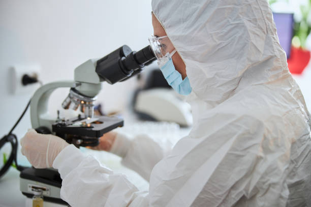 istock Microbiologist in a hazmat suit observing a microscopic specimen 1315369497