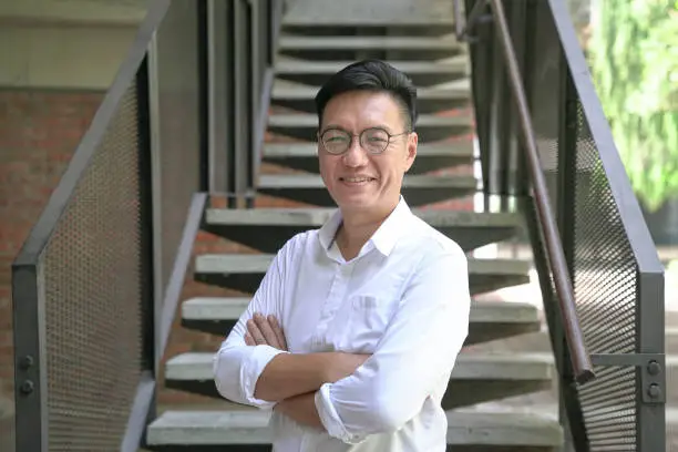 Photo of Portrait of a smiling Asian businessman with arms crossed, wearing white shirt.