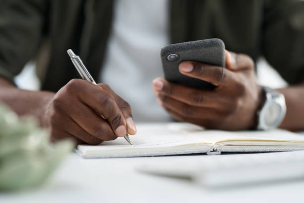 istock Cropped shot of a young man using his phone and writing at work 1315371150