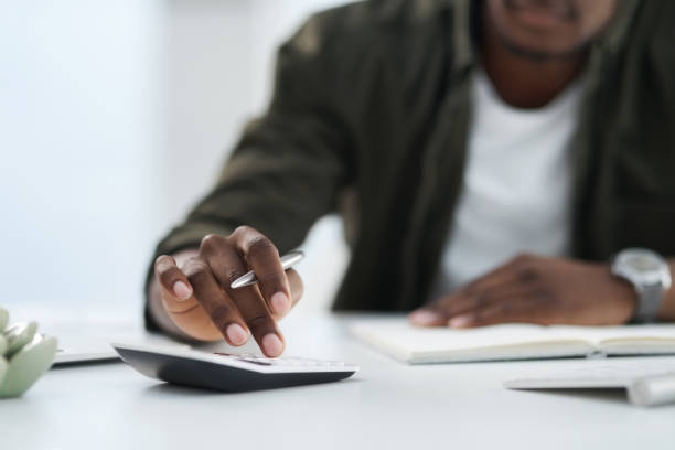 Cropped shot of a young man using a calculator at work Running the numbers revenue photos stock pictures, royalty-free photos & images