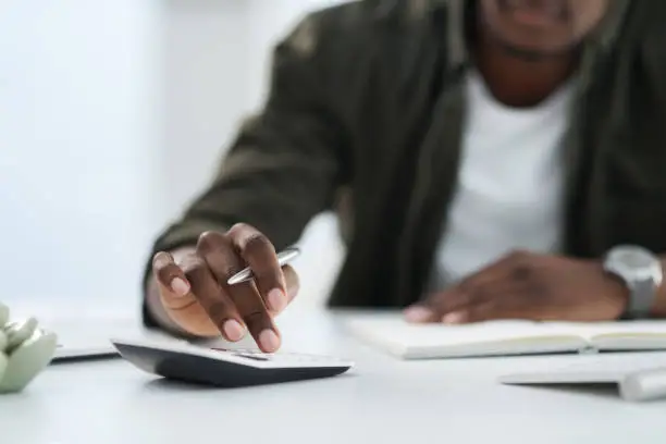 Photo of Cropped shot of a young man using a calculator at work