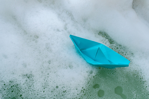 Origami in the form of a paper boat in soapy water in a bath as a hobby and a concept