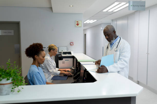 istock Three diverse male and female doctors in hospital reception using computers looking at documentation 1315376402
