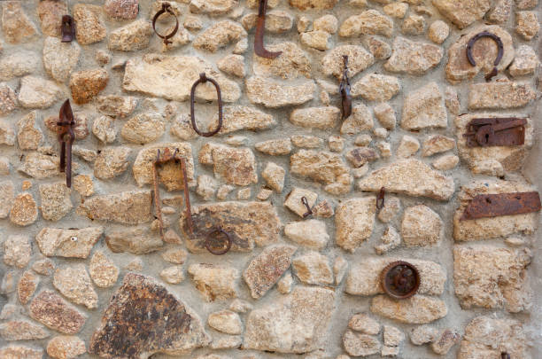 Various old homemade utensils along with rusty tools used in agriculture hanging on the exterior wall of a dwelling in a town