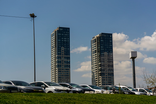 Two skyscrapers, two metal poles and lots of parked cars toward the blue and cloudy sky in Istanbul.