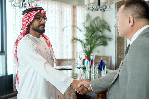 A man in a white robe shaking hands with a man in grey suit after negotiating