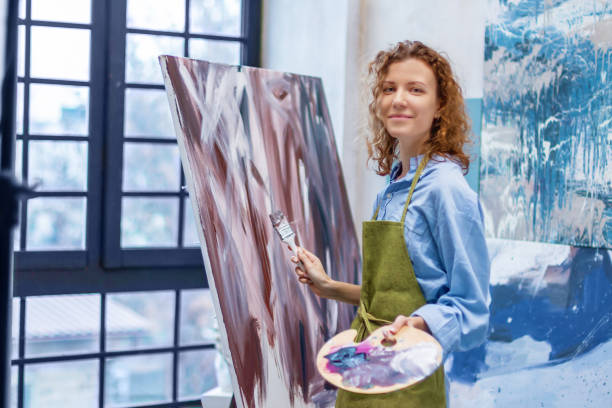 Woman artist drawing on canvas with brush in studio Woman artist is drawing abstract picture standing in her workshop studio gallery. Process of creating brown beige oil, watercolor, acrylic painting at creative workplace. Contemporary modern art. abstract oil painting for beginners stock pictures, royalty-free photos & images