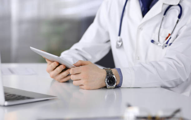 istock Unknown male doctor sitting and working with tablet computer in clinic at his working place, close-up. Young physician at work. Perfect medical service, medicine concept 1315390427