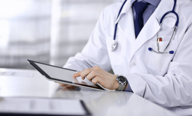 istock Unknown male doctor sitting and working with tablet computer in clinic at his working place, close-up. Young physician at work. Perfect medical service, medicine concept 1315390450