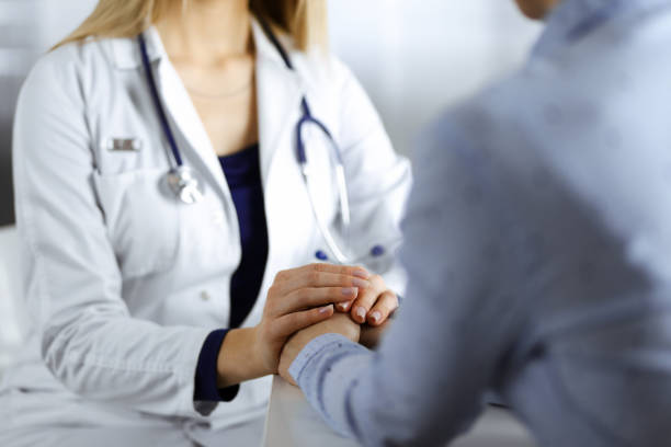 Unknown woman-doctor is holding her patient's hands to reassure the patient, discussing current health examination, while they are sitting together at the desk in the cabinet in a clinic. Female physician with a stethscope at work, close-up. Perfect medical service in a hospital. Medicine concept. una mujer-médico desconocida está sosteniendo las manos de su paciente para tranquilizar a la paciente, discutiendo el examen de salud actual, mientras están sentados juntos en el escritorio del gabinete en una clínica. médico con un estetoscopio en e