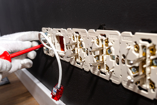 A network cable protruding from the wall with a ready RJ45 module to the computer socket in the room, visible electrical sockets.