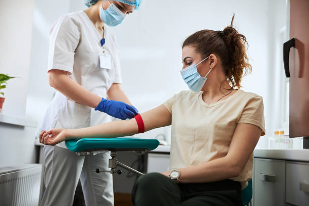 Experienced phlebotomist preparing a woman for blood draw Skilled focused young phlebotomy technician applying a tourniquet to a female patient arm for venipuncture blood stock pictures, royalty-free photos & images