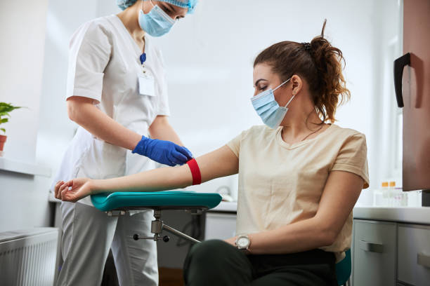 Experienced phlebotomist preparing a woman for blood draw Skilled focused young phlebotomy technician applying a tourniquet to a female patient arm for venipuncture biology lab stock pictures, royalty-free photos & images