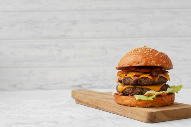 istock Double cheeseburger served on wooden board against white blurred background 1315402334