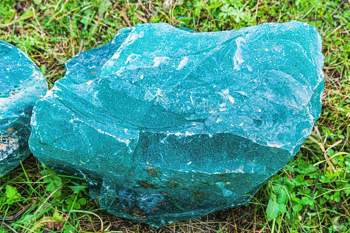 Decorative antique block of glass. A glass cobblestone lies on the grass. The stone is in an old abandoned glass factory.