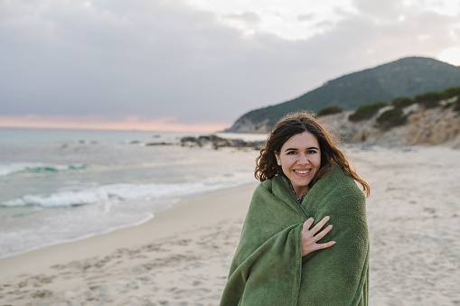 Portrait of Young attractive woman looking at the camera on the beach shore wearing a blanket