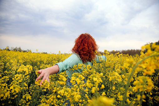 Happy smiling young woman with outstretched arms posing in an oilseed or canola field. About 25 years, female Caucasian redhead.