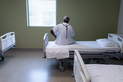 Portrait of african american male patient sitting on hospital bed looking through the window. medicine, health and healthcare services.