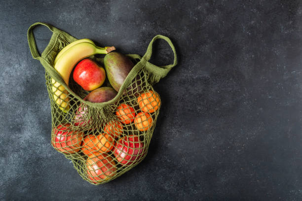 istock Fresh fruit in a green string bag on a black background. Bananas, apples, oranges, and mangoes. 1315422646