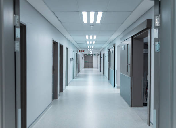 istock Empty, clean white corridor in modern hospital with overhead lighting, lined with doors 1315427642