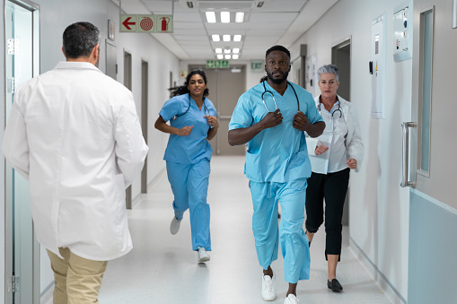 Diverse group of male and female doctors running through busy hospital corridor. medicine, health and healthcare services.