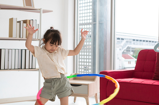 Happy Asian girl playing Hula Hoop in the living room at home. Young little girl learning to play with a hula-hoop in a living room.