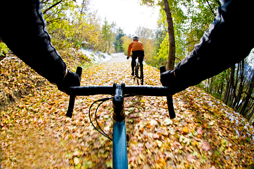 The handlebar view of two men going for a gravel bicycle ride on a rail grade trail in October. Gravel bikes are similar to cyclo-cross bikes with tires suited for riding on rough terrain.