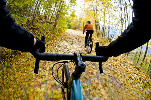 The handlebar view of two men going for a gravel bike ride on a rail grade trail in October. Gravel bicycles are similar to cyclo-cross bikes with tires suited for riding on rough terrain.