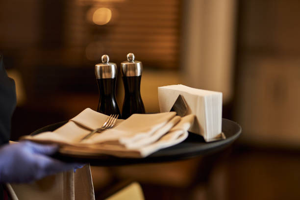 Cropped photo of hand in glove holding a waiter tray with condiments and silverware