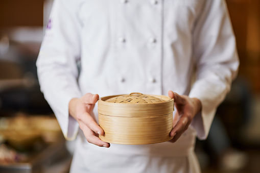 Cropped photo of chef in perfectly wite uniform holding a bamboo container