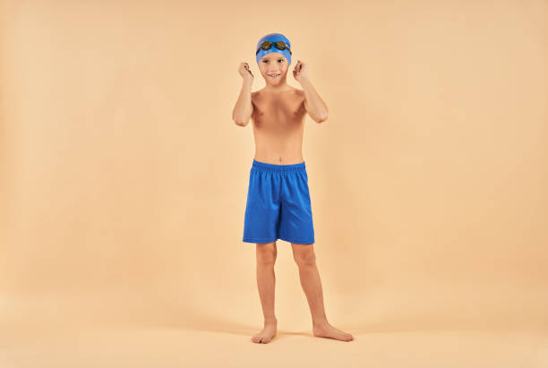 istock Cute boy swimmer standing against light orange background 1315444367