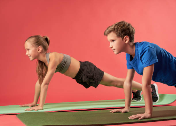 istock Adorable girl and boy doing plank against red background 1315444381