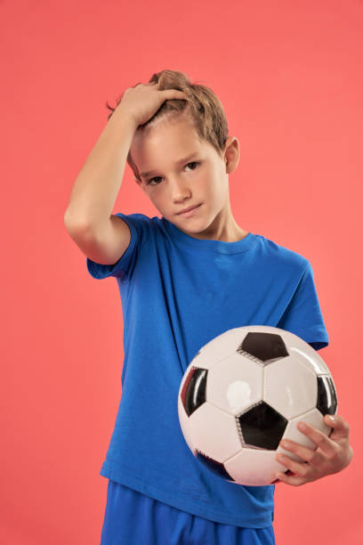 istock Cute boy with soccer ball standing against red background 1315444941