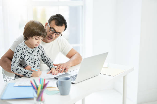 istock Help your child. Loving latin father playing with his son. Businessman using laptop while working from home and watching child 1315445122