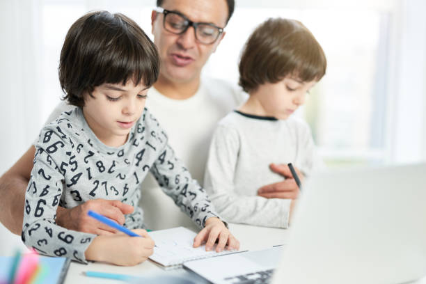 istock Teach your child. Cute little latin boy drawing while spending time with his dad and brother at home. Businessman using laptop while working from home and watching children 1315445139