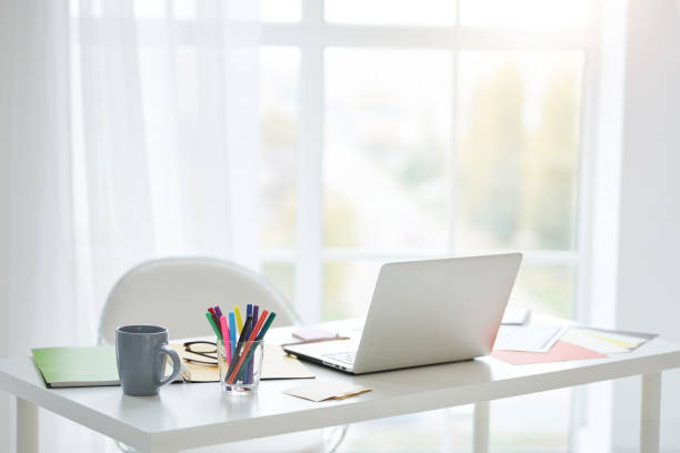istock Home office. Workplace with white laptop, notes and cup of tea on the table at home. Bright light coming from the window 1315445791