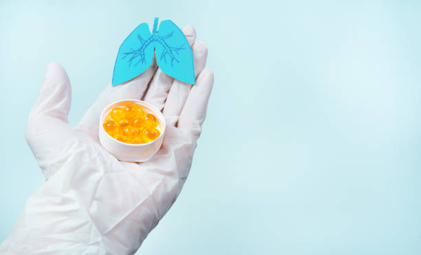 Paper lungs and white pills on doctorâs gloved hand, blue background. Omega-3 supplements help fight coronavirus and lung disease stock photo