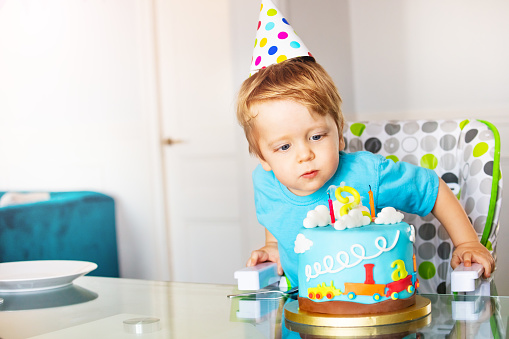 Little two year old toddler blow candles birthday cake wearing party cap