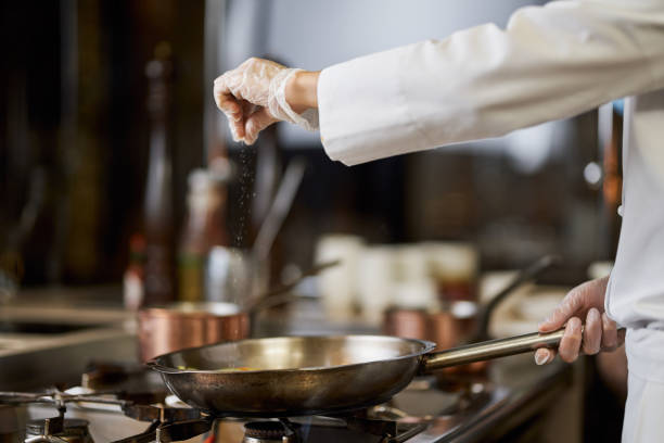 istock Chef in white uniform salting his cooking in the pan 1315450121