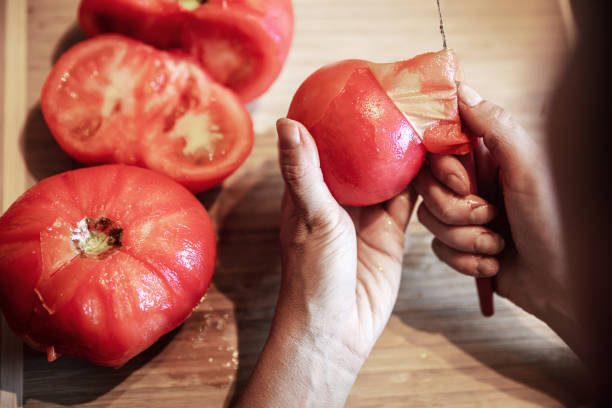 une femme épluche beaucoup de tomates rouges fraîches et bouillies avec un couteau, se préparant à la cuisson d’une sauce - épluché photos et images de collection