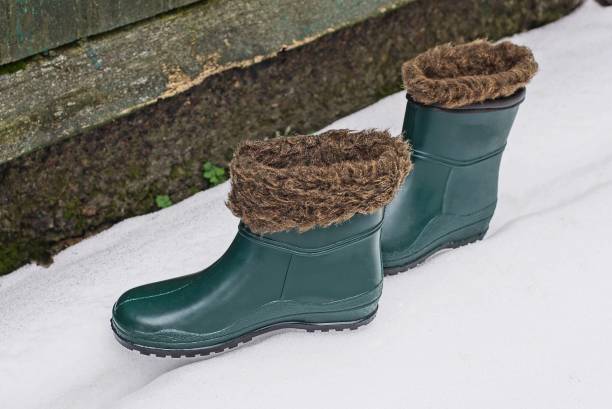 zwei gummi winter grüne stiefel mit braunem fell auf weißem schnee - snow track human foot steps stock-fotos und bilder