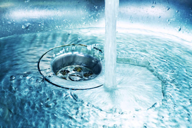 una corriente de agua limpia fluye hacia el fregadero de acero inoxidable en tonos azules. - sink drain plumber domestic kitchen fotografías e imágenes de stock