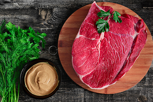 piece of raw meat - uncooked juicy steak on wooden board on wooden table flat lay mustard and parsley