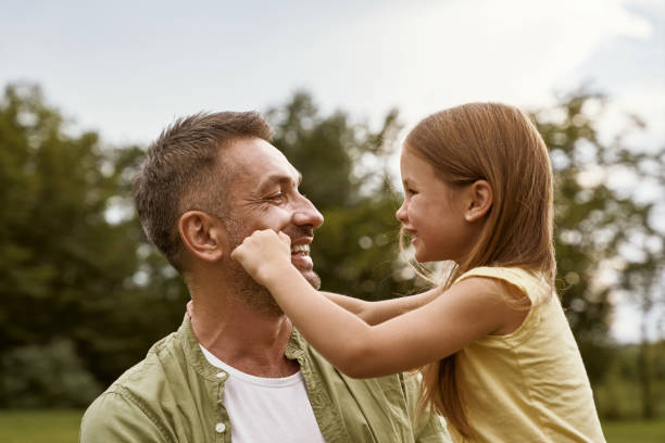 istock Fathers day. Cute little girl playing with her daddy while visiting park on a summer day, touching his cheeks and smiling 1315463787