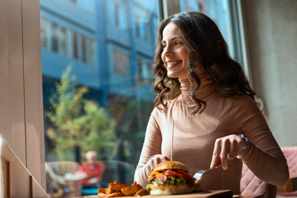 istock Young woman eating burger looking through window smiling 1315472366